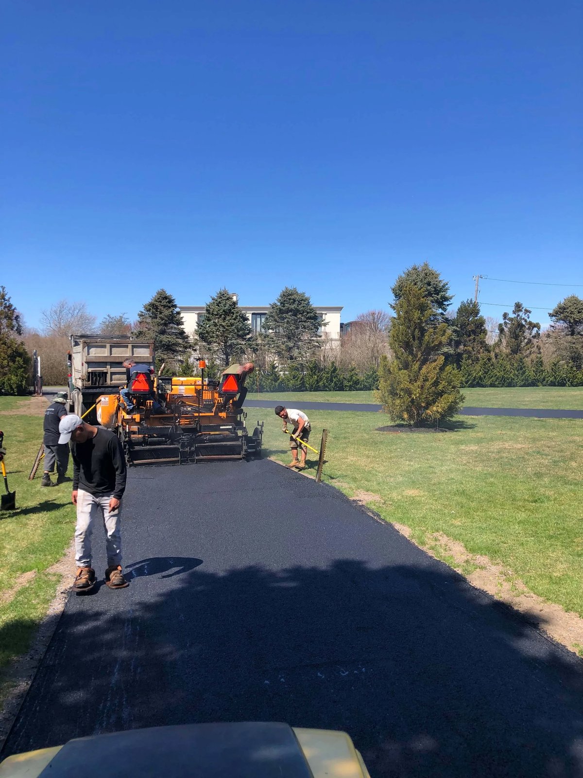 Paving crew laying a fresh asphalt driveway with a paver and dump truck on a clear day