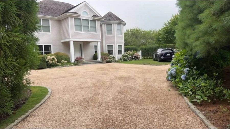 Finished pea gravel driveway leading to a white two-story house framed by landscaping