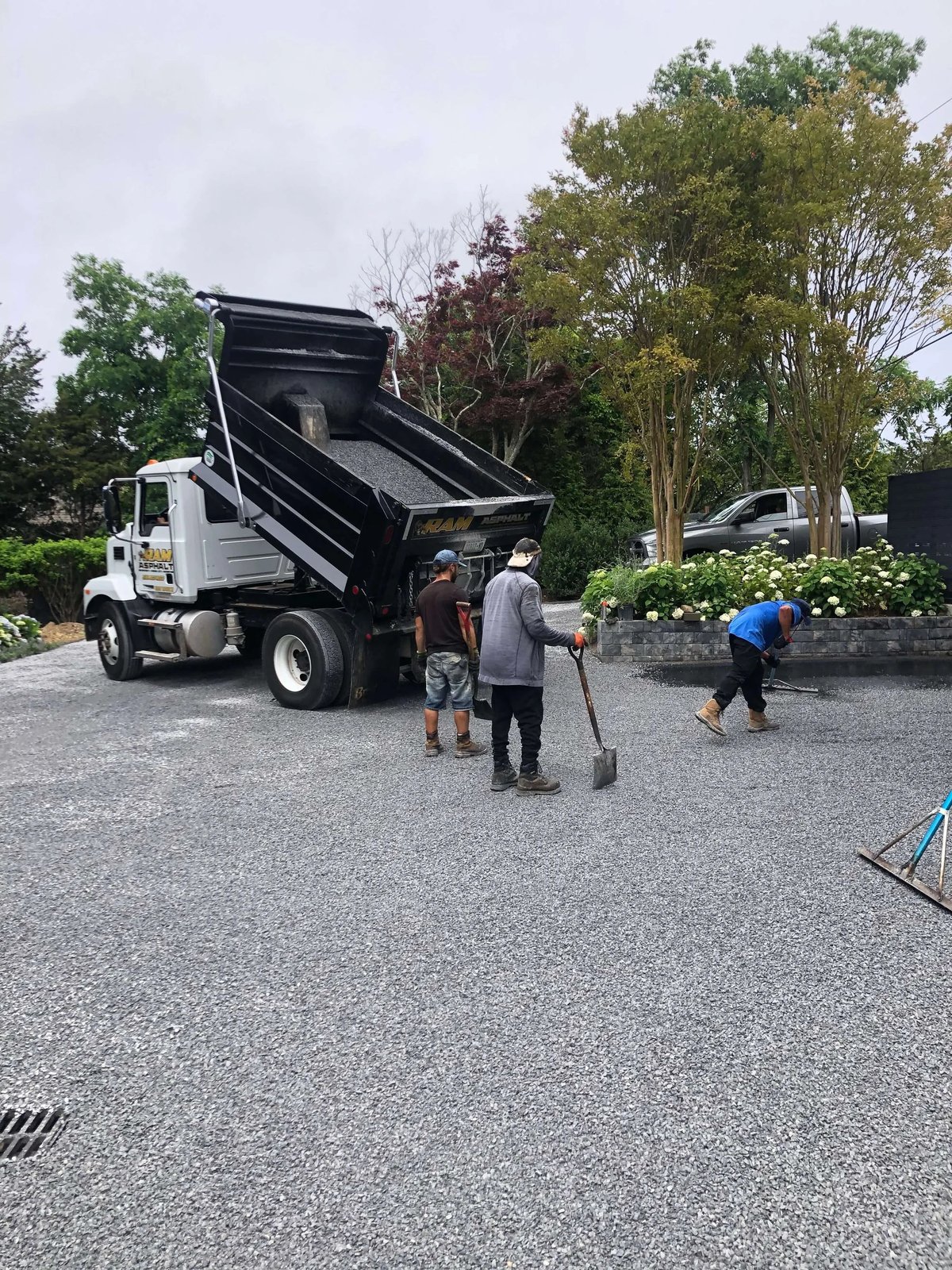 Dump truck spreading crushed stone while the crew rakes a new gravel driveway